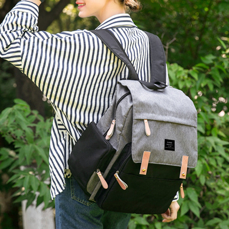 Woman mom carrying a gray baby diaper backpack outdoors with greenery in the background