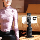 Phone holder with 360-degree rotation and face tracking on a table, blurred person in the background. 