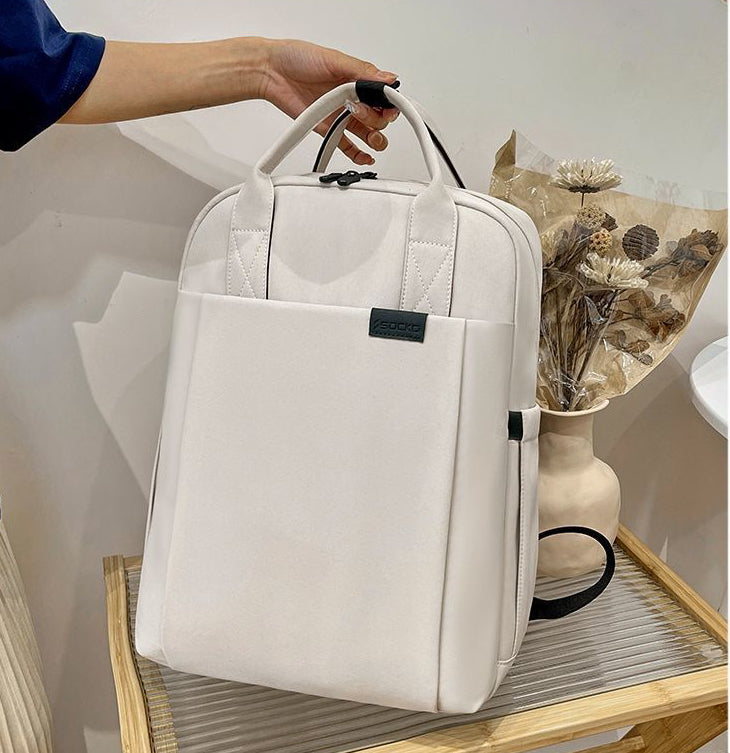 Beige backpack held by a female hand on a wooden surface with a vase and flowers in the background