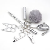 8-piece women’s self-defense keychain set in silver, including alarm, self-defense stick, window breaker, whistle, knife, knuckle tool, bottle holder, and pompom—all arranged neatly for display.