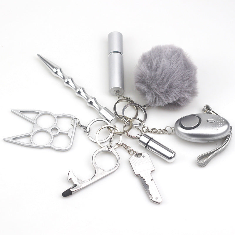 8-piece women’s self-defense keychain set in silver, including alarm, self-defense stick, window breaker, whistle, knife, knuckle tool, bottle holder, and pompom—all arranged neatly for display.