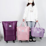 Woman holding three travel bags of different colors on wheels against a plain background. Expandable tote bag with removable wheels in pink, purple, large travel bag with waterproof compartments, dry/wet separation, and up to 75L capacity, shown in travel-ready style.”
