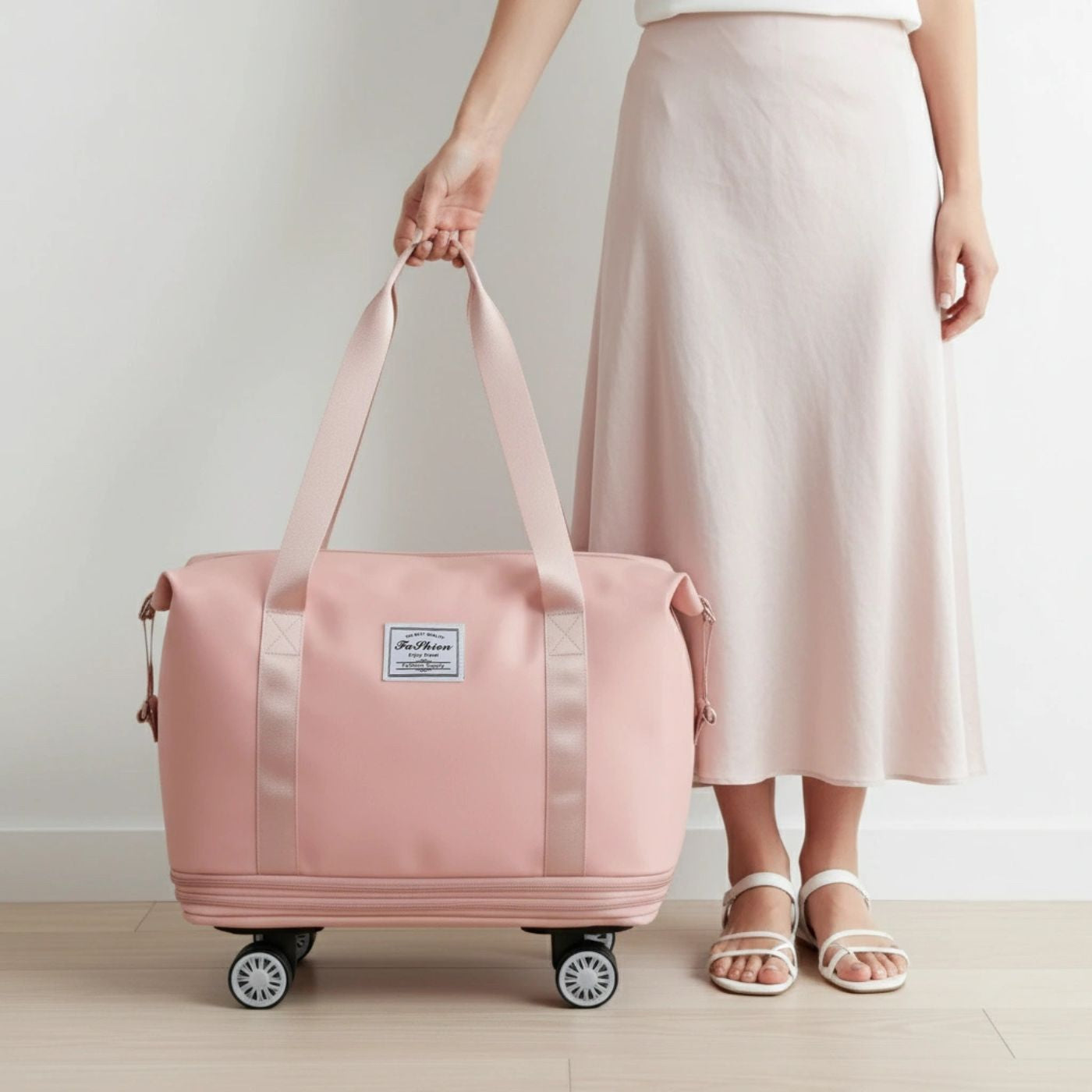 Person holding a pink travel bag with wheels on a light wooden floor. Expandable tote bag with removable wheels in pink, large travel bag with waterproof compartments, dry/wet separation, and up to 75L capacity, shown in travel-ready style.