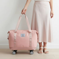 Person holding a pink travel bag with wheels on a light wooden floor. Expandable tote bag with removable wheels in pink, large travel bag with waterproof compartments, dry/wet separation, and up to 75L capacity, shown in travel-ready style.
