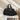 Black quilted duffel bag on a white surface with a beige wall and dried plants in the background