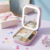 Pink makeup case with LED mirror and cosmetic items on a light purple surface with gift boxes and flowers.