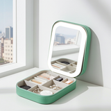 Green makeup box with LED mirror on a white surface near a window with cityscape view