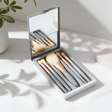 Set of sleek gray mini makeup brushes in a compact case with a mirror on a light surface.
