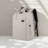 White minimalistic backpack with black straps on a light surface with shadows