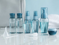A set of refillable cosmetic containers in blue and clear colors, including various sizes with pump and spray nozzles, intended for travel use.