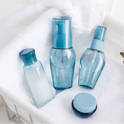 Set of aesthetic refillable blue travel skincare bottles with towels and plants on a light background. A set of refillable cosmetic containers in blue and clear colors, including various sizes with pump and spray nozzles, intended for travel use.