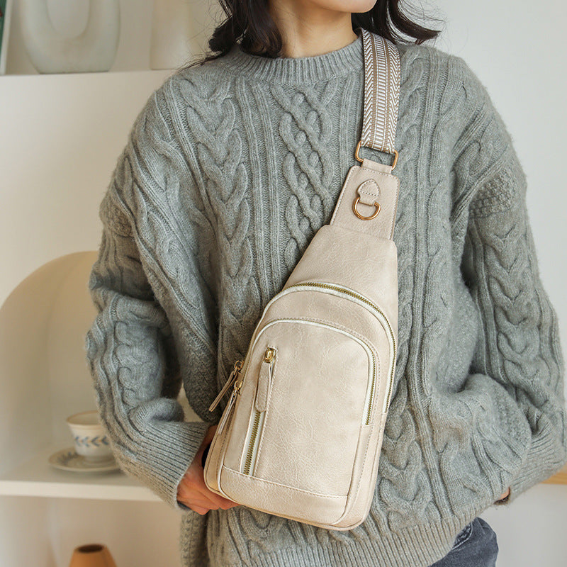 Woman carrying a beige cross body sling bag over one shoulder wearing a white coat by the airport