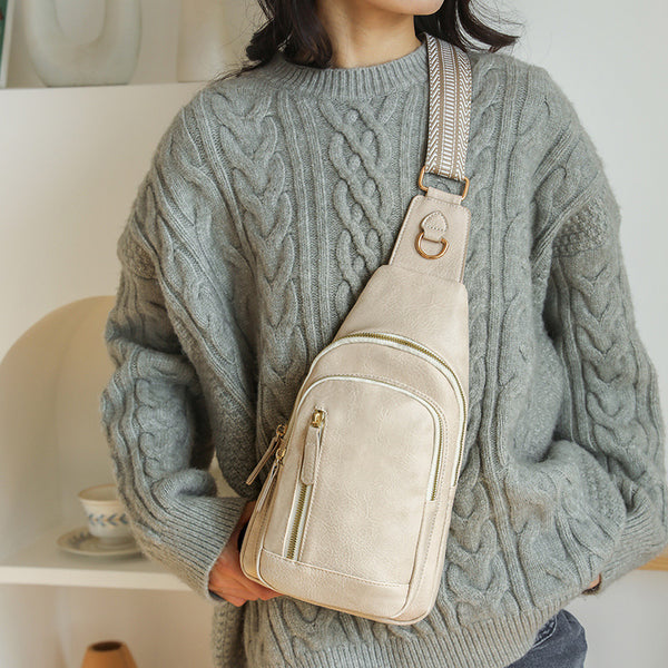 Woman carrying a beige cross body sling bag over one shoulder wearing a white coat by the airport