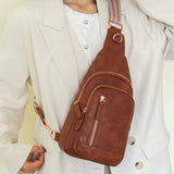 Woman carrying a brown cross body sling bag over one shoulder wearing a white coat by the airport