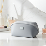 Gray cosmetic bag on a bathroom counter with perfumes in the background