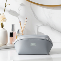 Gray travel cosmetic organizer bag on a vanity with skincare products and a mirror in the background