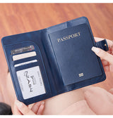 Woman holding a blue travel wallet passport cover with airplane emblem held by a hand against a neutral background