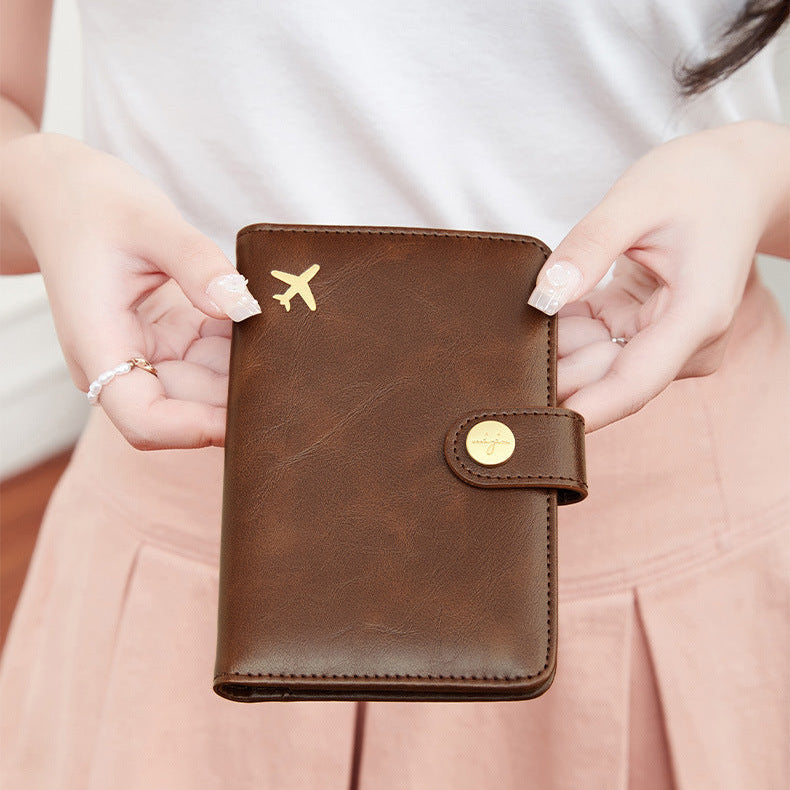 Woman holding a Brown travel wallet passport cover with airplane emblem held by a hand against a neutral background
