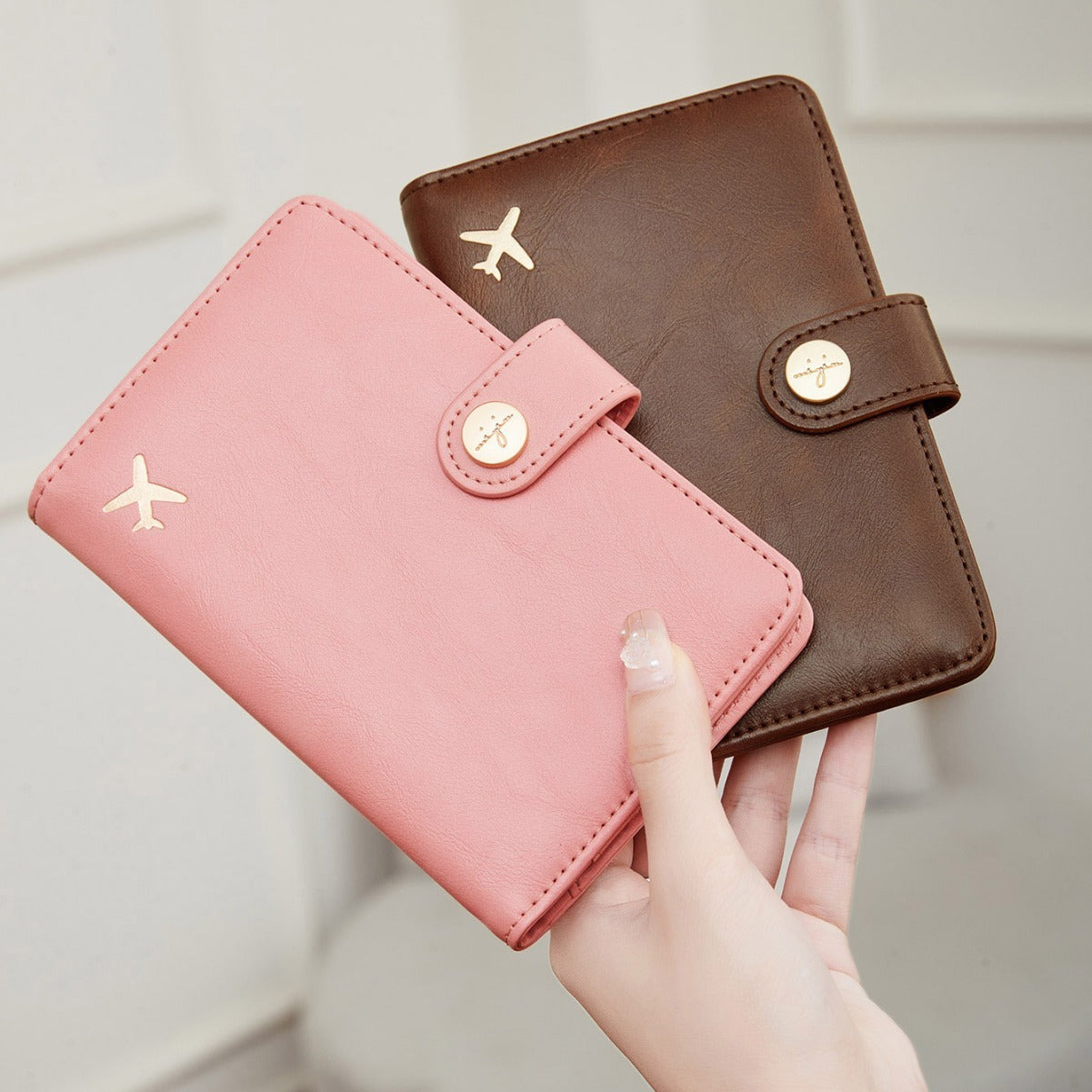 Pink and brown travel wallet passport covers with airplane emblem held by a hand against a neutral background