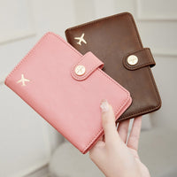 Pink and brown travel wallet passport covers with airplane emblem held by a hand against a neutral background