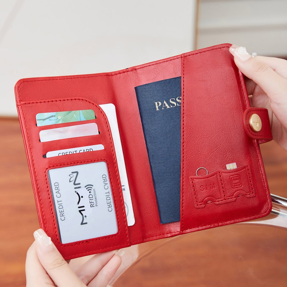 Woman holding a red travel wallet passport cover with airplane emblem held by a hand against a neutral background