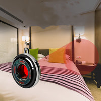 A black candid camera detector with blue details in the center, designed to look like coins. The device detects a camera hidden next to a hotel bed and is used for personal safety and privacy