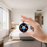A wireless candid camera detector with a compact, circular design featuring a blue indicator dial and black exterior. A woman's hand holding the detector up, with a clean minimalistic Scandinavian style hotel room  backdrop.