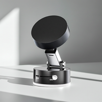 Foldable magnetic phone holder in black, combining vacuum suction and magnetic grip, compatible with most smartphones, shown mounted on dashboard for hands-free use.