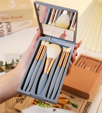Set of makeup brushes in a gray case held by a female hand on a magazine background