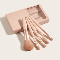 A set of five mini makeup brushes in various shapes and sizes, displayed alongside a small open mirror box in a matching soft pink color.