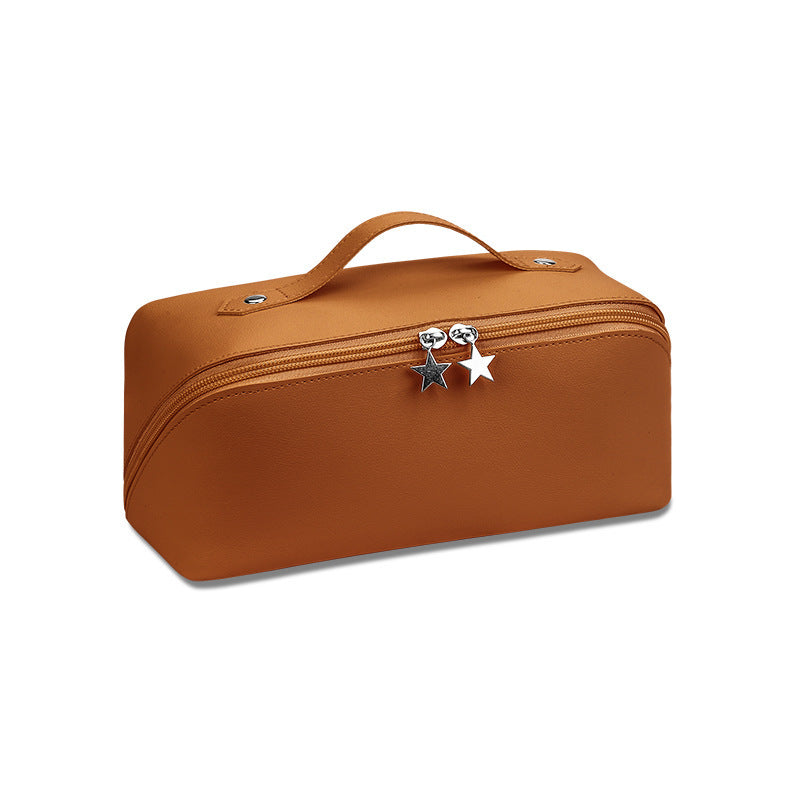 A cosmetics beauty travel organizer in a brown camel color with a zipper closure and a decorative star charm.