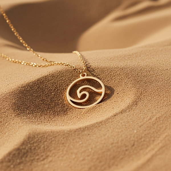 Minimalistic gold stainless steel necklace with an ocean wave pendant on soft sand