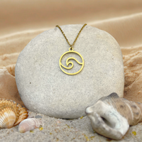 Minimalistic gold stainless steel wave pendant necklace on a stone with seashells and sand in the background