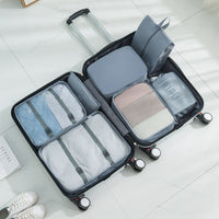 Open suitcase with gray packing cubes organizers inside on a light wooden floor.
