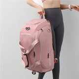 A woman holding a large capacity sports travel bag in pink color with multiple compartments, featuring a shoulder strap and the text 'SPORT' on the front.