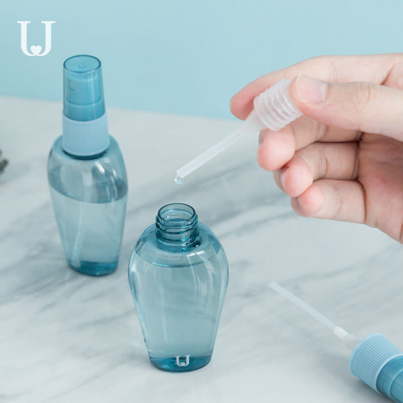 A set of refillable cosmetic containers in blue and clear colors, including various sizes with pump and spray nozzles, intended for travel use.