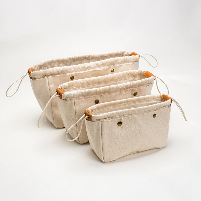 Three beige cotton canvas bag organizers with different sizes displayed against a white background. Beige cotton canvas bag organizer with multiple pockets, Japanese minimalist design, available in drawstring or zipper closure, shown in small/medium/large sizes.