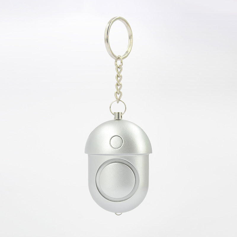 A compact mini self-defense alarm with a keychain, featuring a silver color and a dome shape with a central button.